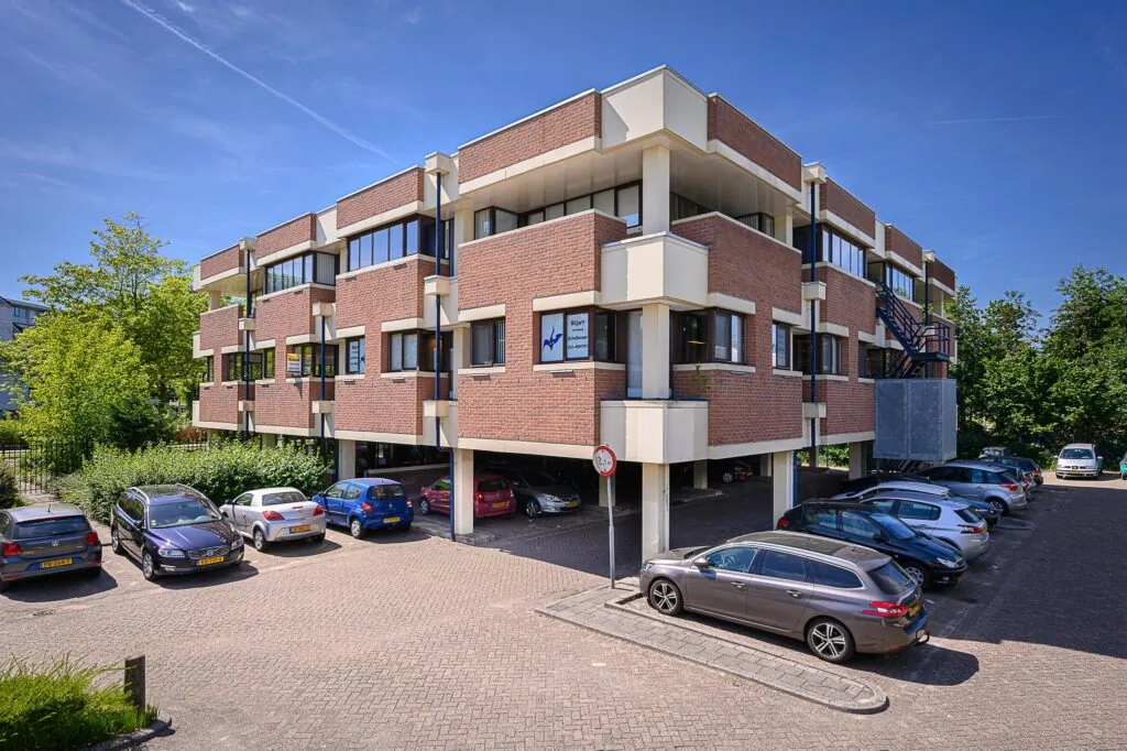 Bakstenen kantoorgebouw De Linie met parkeerplaatsen ervoor op een zonnige dag.